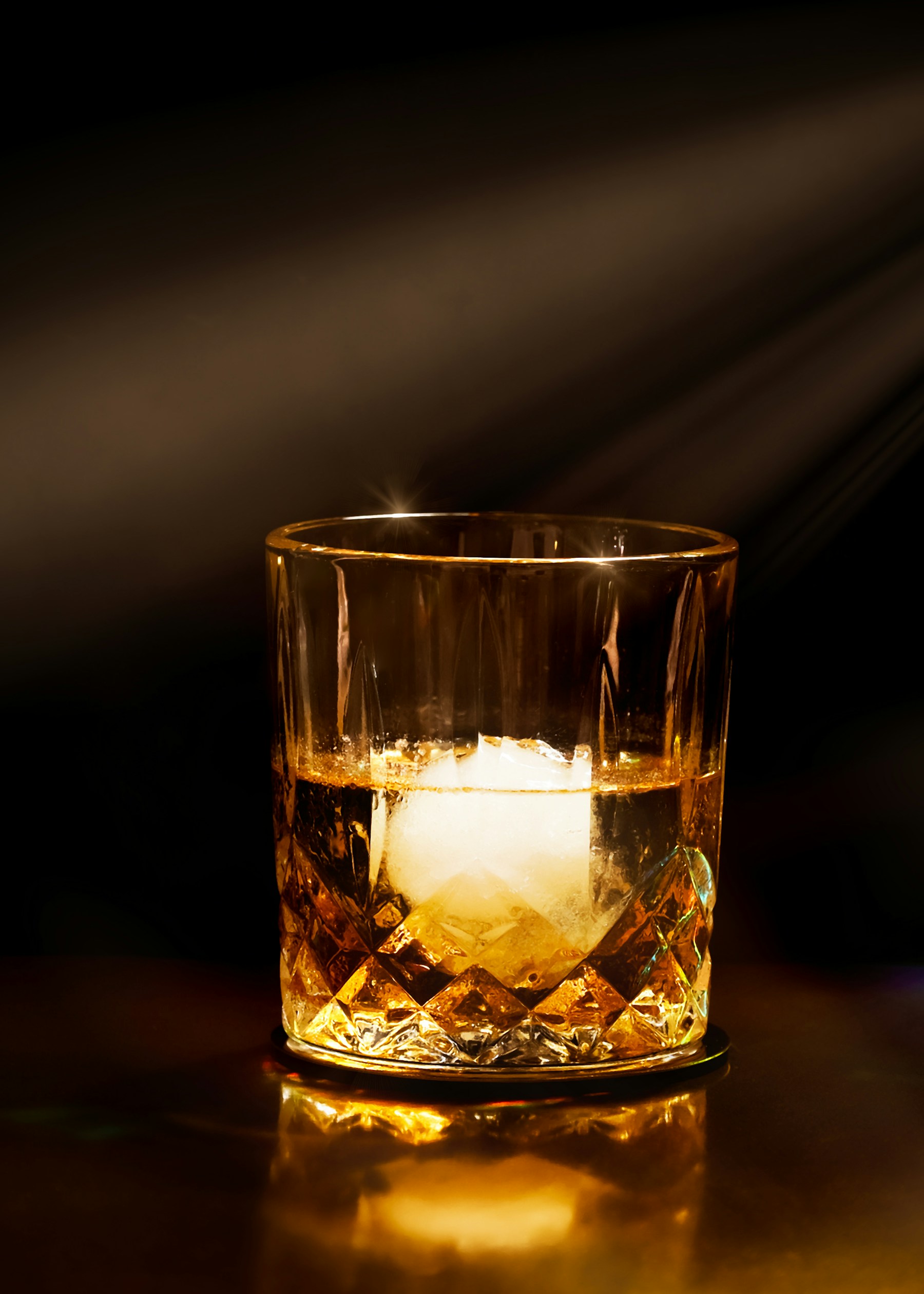 Amber whiskey with ice in a crystal glass against a dark background